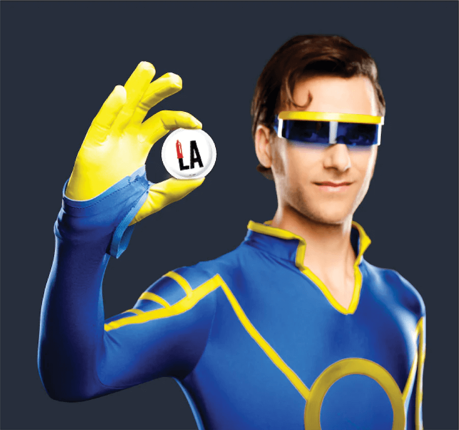 Person in superhero costume holding a 'LA' badge against a dark background