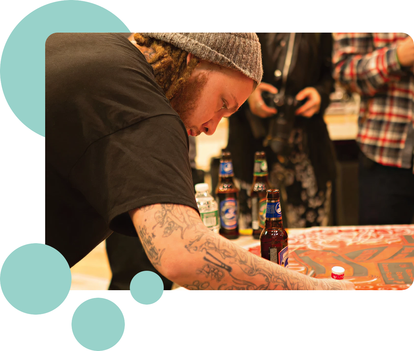 Person with tattoos at a table with beer bottles, surrounded by teal circles