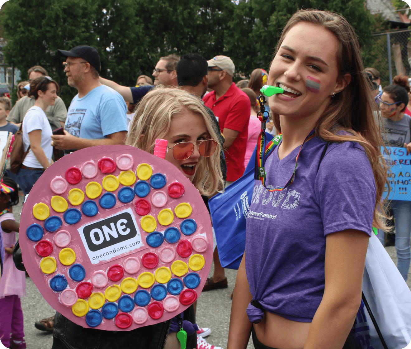 Two people at a public event with colorful face paint and a large candy-themed prop.