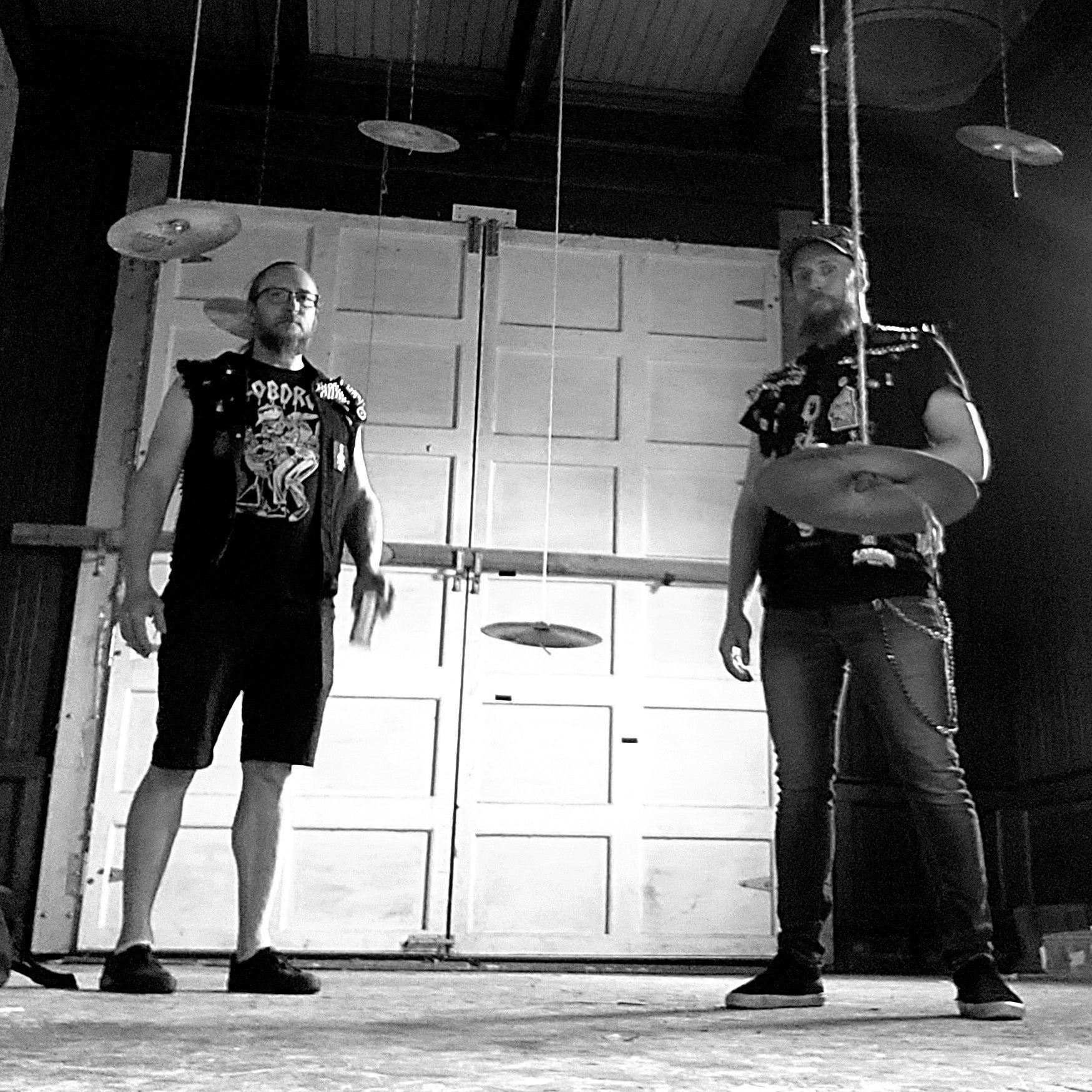 Two individuals standing in a room with musical instruments, possibly in a studio or rehearsal space.